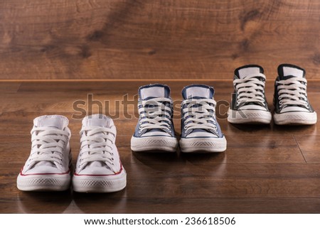 three pairs of cool youth white gym shoes with red  stripes  on brown wooden floor  standing in line with perspective