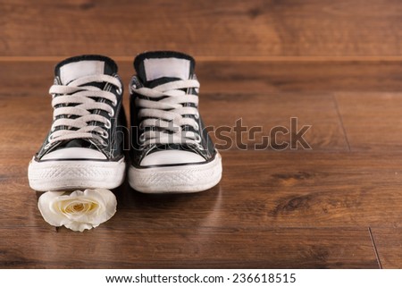 pair of  cool youth white black  gym shoes stepping on  white rose on brown parquet  wooden floor