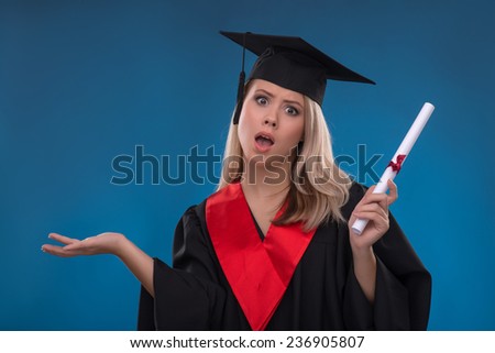 Portrait of beautiful disappointed  blond girl in black cloak and master hat holding bundle of sheet of paper on blue background looking at camera