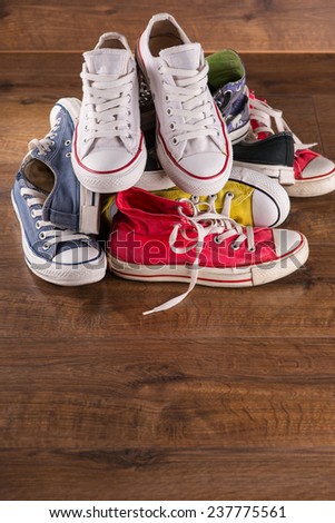 heap of several  pairs of cool youth red blue white yellow  gym shoes   on brown wooden floor  with copy place