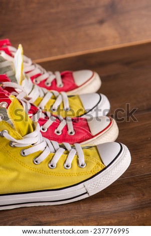 two pairs of cool youth red and yellow  gym shoes white laces   on brown wooden floor  standing in line side view