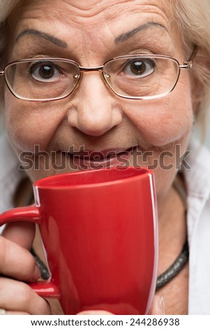 Enjoying the cup of coffee. Cropped image of happy senior woman smelling the cup of coffee looking at camera while standing against grey background