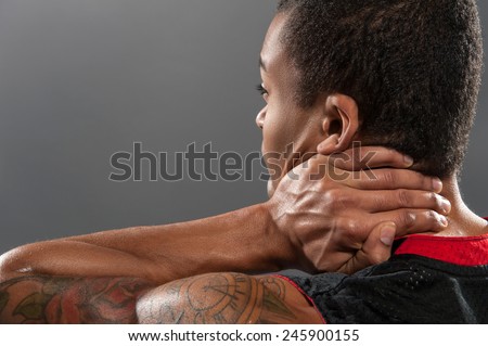 Feeling neckache after workout. Frustrated young African man touching his neck from behind and expressing negativity while standing against grey background