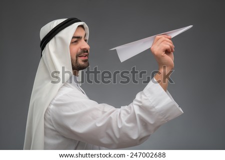 Unlimited business opportunities. Cheerful Arab businessman holding an airplane and looking away while standing against grey background