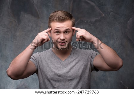 Use your brain. Young handsome man keeping his fingers on his temples while standing on dark background