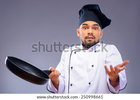 Not sure in his result. Closeup portrait of handsome cook holding a frying pan and stretching out his hands while standing against grey background with copy space