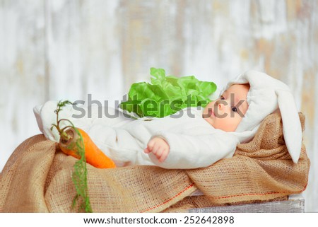 Cute little bunny. Conceptual side view of a little baby in a bunny bodysuit lying in the basket with green cabbage and carrot