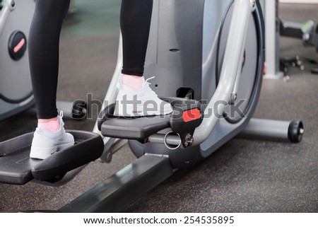 Fitness gym workout. Cropped image of young beautiful woman in sports clothing doing exercises in the gym on elliptical cross trainer