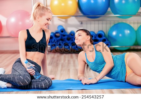 Fun in aerobics class. Two beautiful young women in sports clothing sitting on the yoga mat and chatting after exercising together