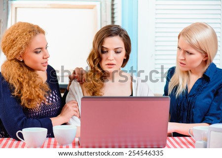 Bad news. Beautiful depressed young woman looking at her laptop while her best female friends comporting her in the cafe