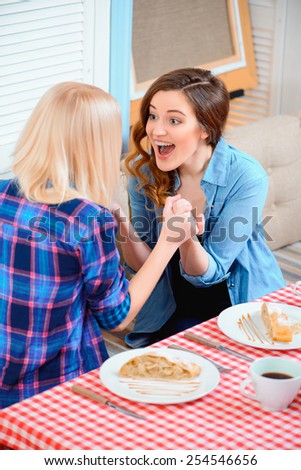So happy for you. Top view of two young beautiful female friends sitting in cafe and holding hands while discussing some exciting news