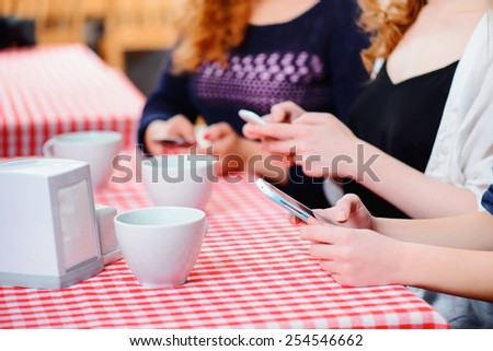 No minute without technologies. Closeup image of three young beautiful female friends sitting in cafe and printing sms on their smartphones