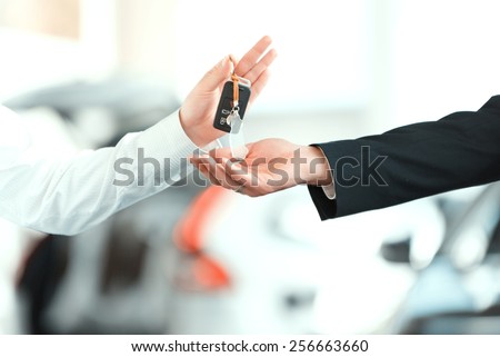 Here is your key. Closeup of man giving key to the car owner while standing in front of a car