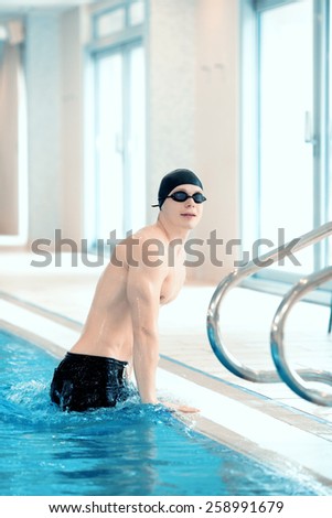 Endurance swimming. Side view of young handsome man wearing a swimming cap going out the pool