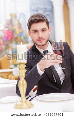 Making a toast. Handsome young man in suit raising his glass of wine while making a toast in luxury restaurant