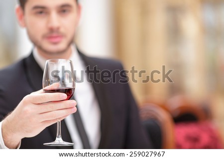 Making a toast. Handsome young man in suit raising his glass of wine while making a toast in luxury restaurant with selective focus