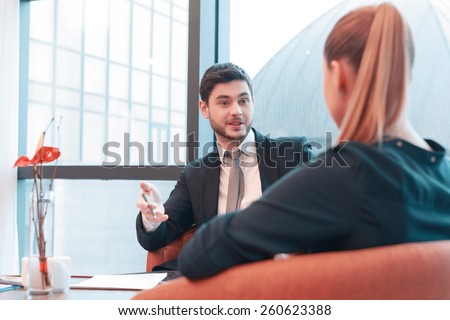 Colleagues at the meeting. Image of handsome young man in formalwear communicating with his female colleague while sitting in the lobby of business center