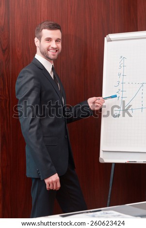 Great presentation. Handsome man in suit and necktie standing near whiteboard and pointing it with smile