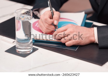 Businessman on business meeting. Cropped image of business man in formalwear holding a pen while sitting at the table with a glass of water