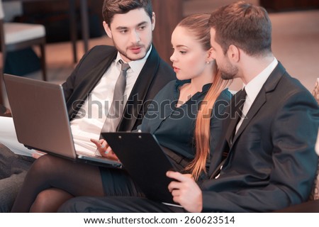 Business team brainstorming. Group of business people in formal wear sitting together on the couch and discussing something while looking at the laptop