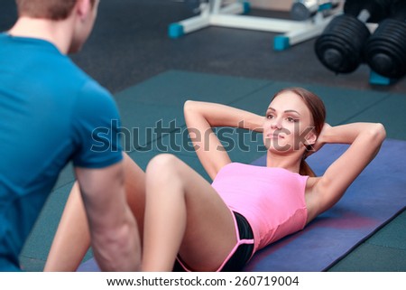 Confident trainer. Concentrated young beautiful woman in sports clothing doing abdominals on the bench in the gym with her sports trainer