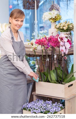 Flowers are my passion. Portrait of a beautiful florist surrounded by flowers in her place of work and cleaning the floral box with a napkin