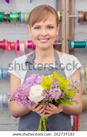 Making a success of her skills. Young smiling florist showing a pretty floral bouquet being completed
