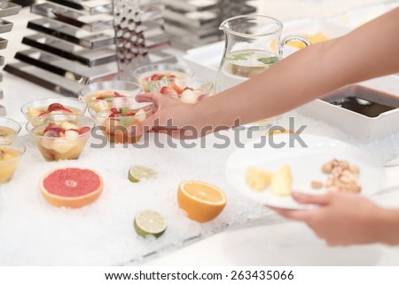 Cannot stop eating sweet desserts. Cropped view of the female hands taking fruit desserts in a glass from buffet table