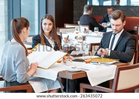 Need to control timing of the meeting. Businesswomen at the lunch table look at other and their male colleague looks at the watch to check the time