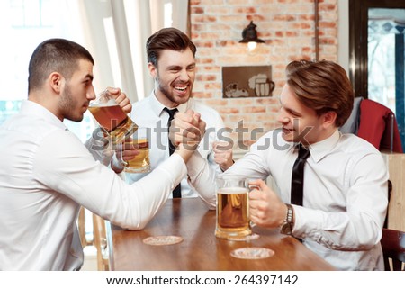 Who is stronger. Three business men wrestling while having a pint of beer on the counter of the bar