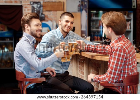 Old friends meeting. Three cheerful young men in casual wear toasting with beer