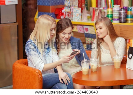 Surfing in the Internet. Three pretty shopping women looking into the screen of the smartphone and discussing something while they sit in a cafe