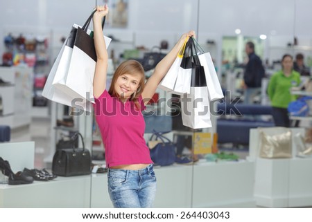 Wow shopping. Young cheerful girl in casual clothes raises her hands with shopping bags