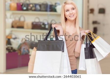 Happy shopping. Smiling and dreamy blond woman holding shopping bags in a shopping mall