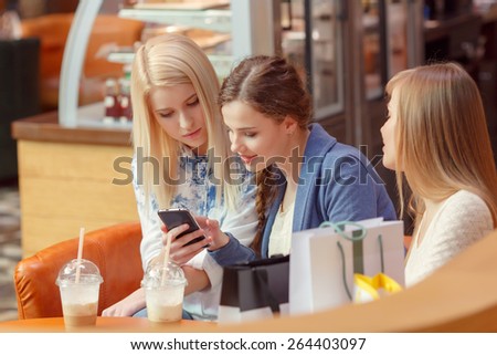Surfing in the Internet. Three pretty shopping women looking into the screen of the smartphone and discussing something while they sit in a cafe