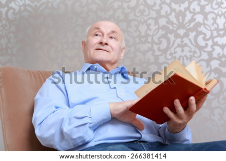 Life memories. Senior man holding a book looks aside as if memorizing something and thinking over the story