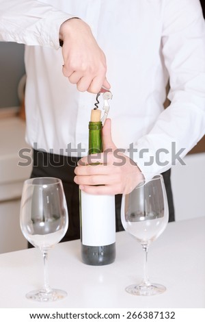 Wine spirit. Close-up of sommelier hands pulling cork from the bottle with two glasses standing by the bottle