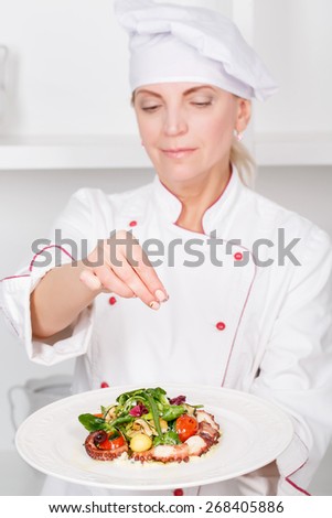 Selective focus on plate with octopus salad and a female cook sprinkling it with spices