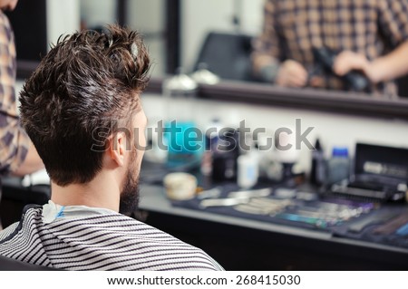 Close-up of a young man with his hair raised upwards sitting before the mirror at barbershop