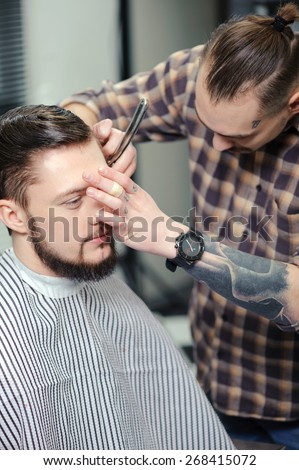 Barber skills. Young stylish experienced barber shaves a client with an old-fashioned straight razor