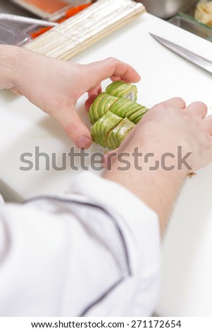 True Japanese meal. Close-up on hands of a cook arranging green sushi rolls with avocado and shrimps