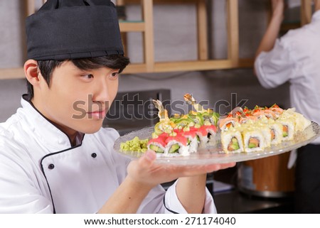 Professional sushi cook. Young Asian cook looking precisely on a plate with various kinds of Japanese rolls