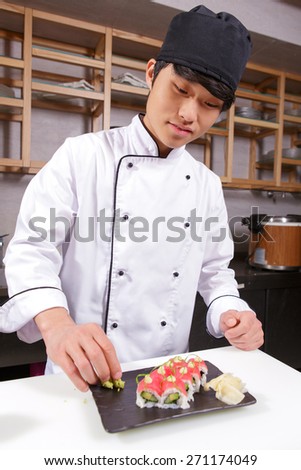 Sushi rolls presentation. Young Japanese cook putting wasabi on a rectangular plate with tuna sushi rolls