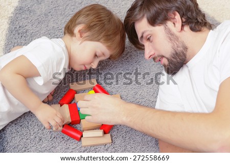 Family interaction. Young handsome father and cute son play building kit lying on a carpet in children room