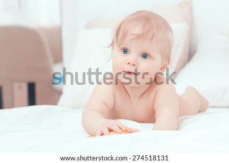 Childhood. Portrait of crawling baby boy on the bed curiously looking behind the camera