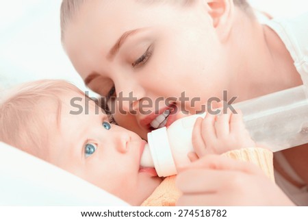 Feeding of a baby. Mother watching and holding her baby eating from the bottle