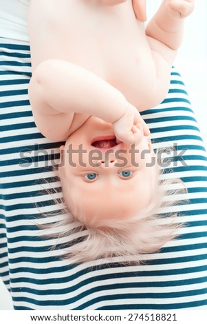 Childish games.  Little baby hanging smiling upside down in front of a stripped skirt of his mother
