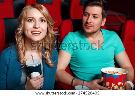 To each his own. Young man and woman in cinema watching film and eating popcorn and drinking coke.