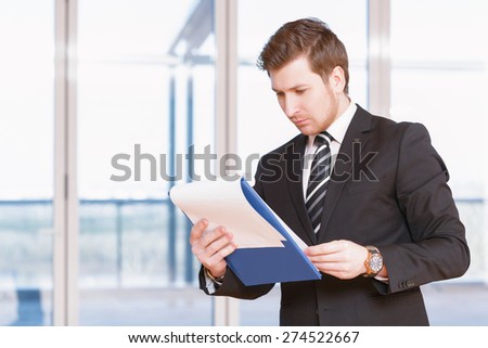 Business plan. Portrait of young businessman standing reflectively and holding the folder studying business plan