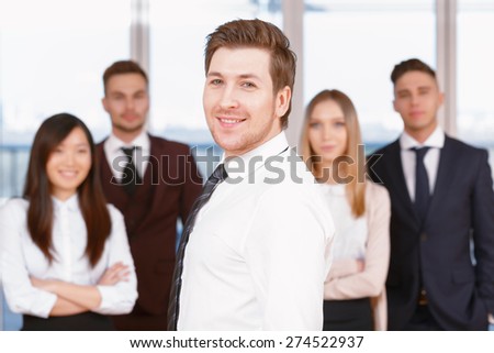 Team in the office. Young handsome businessman standing in the foreground smiling side view , his team of co-workers in the background